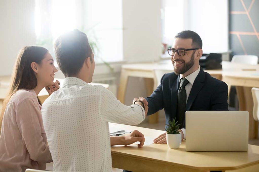 A couple reviews financial documents together at a kitchen table with a calculator and notepad.