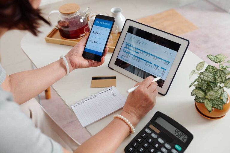A couple sitting at a kitchen table reviewing household bills and a laptop together.